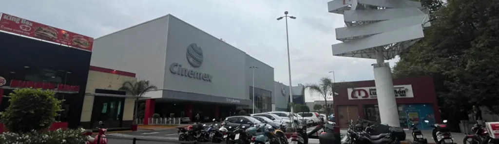 Vista exterior de Cinemex con estacionamiento y anuncios luminosos al atardecer.